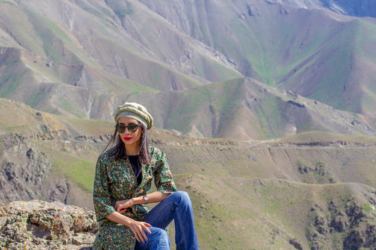 woman in green and black floral long sleeve shirt and blue denim jeans sitting on rock