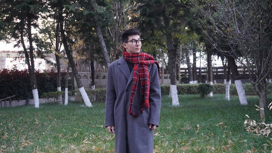 a man standing in a field wearing a coat and a scarf