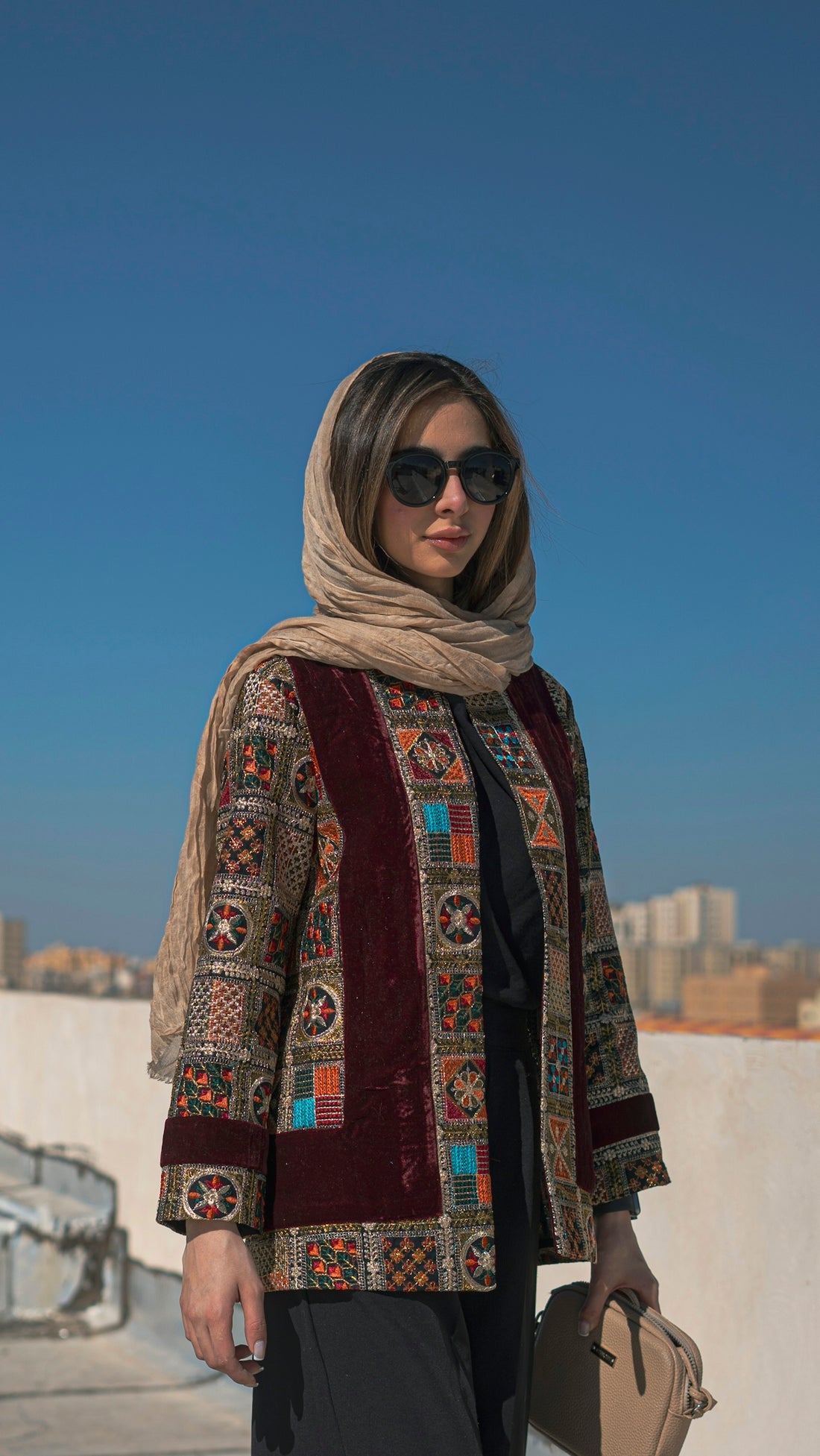 a woman wearing a scarf and sunglasses holding a purse